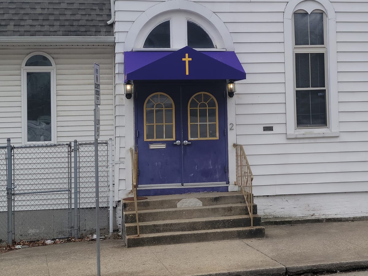 Purple door canopy with a gold cross over the front doors of a white church