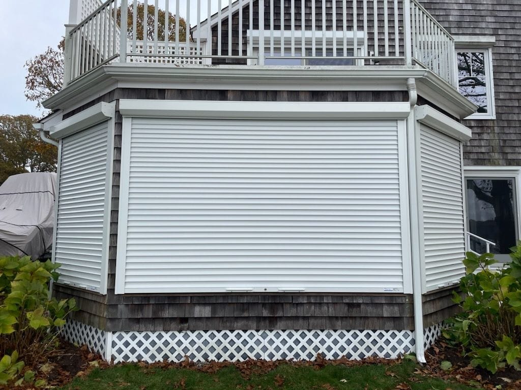 Roll-down hurricane shutters closed over a bay window beneath a second-story deck
