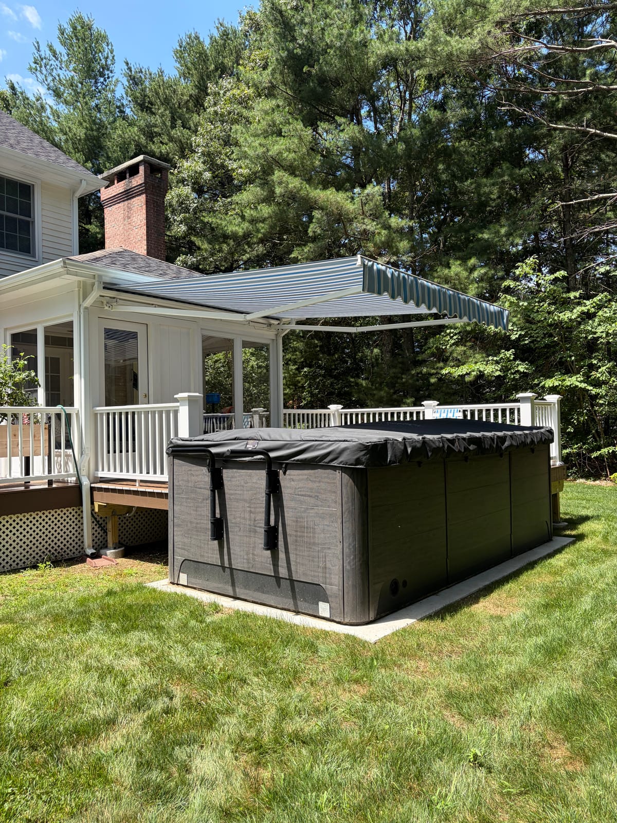Blue striped retractable awning extended over a backyard deck and hot tub