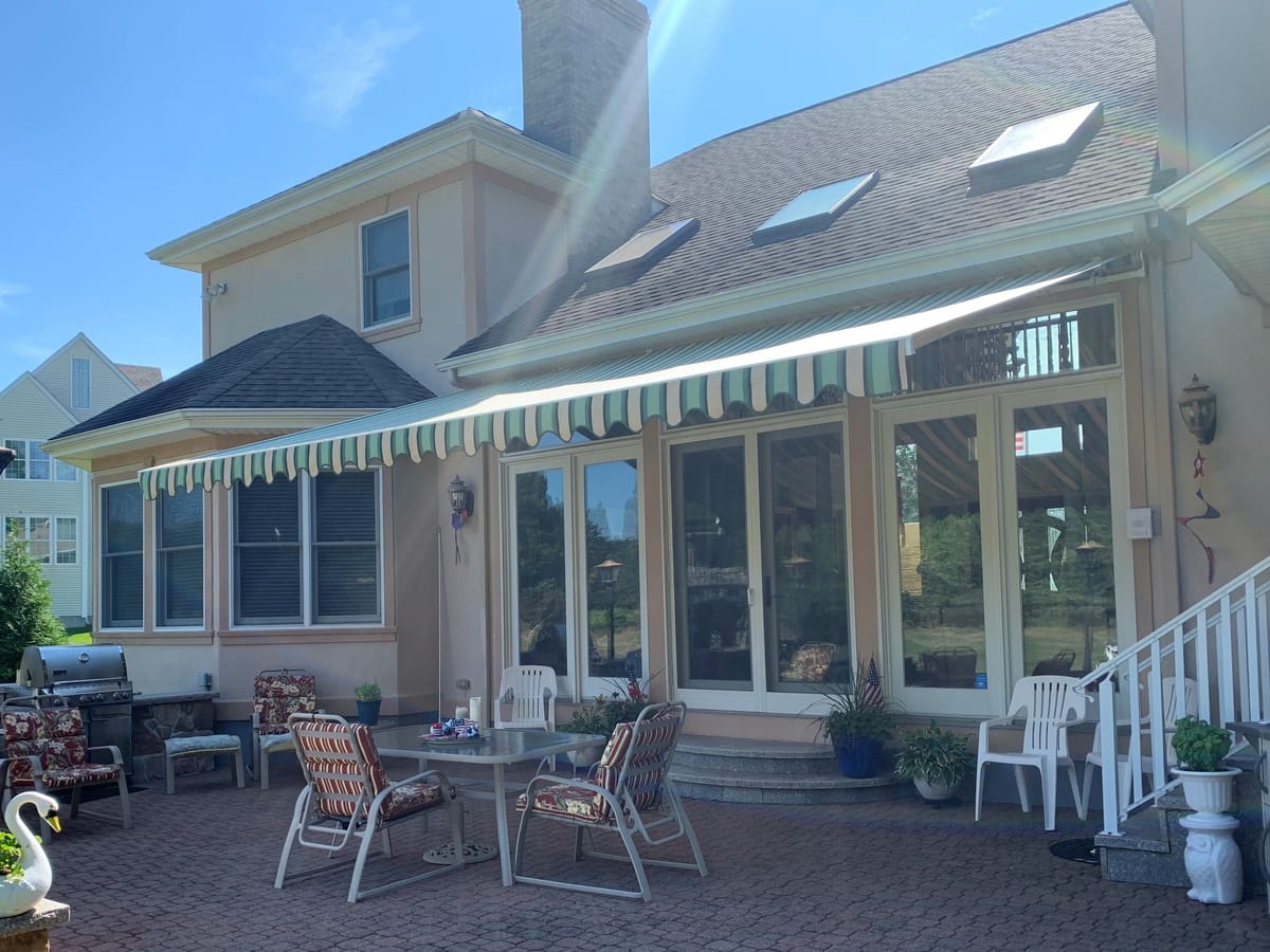 Green striped retractable awning extended over patio doors on a stucco home