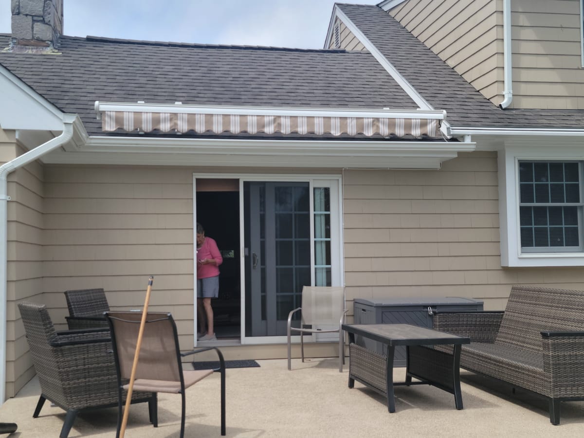 Roof-mounted retractable awning in tan Toga stripe, retracted above a patio door