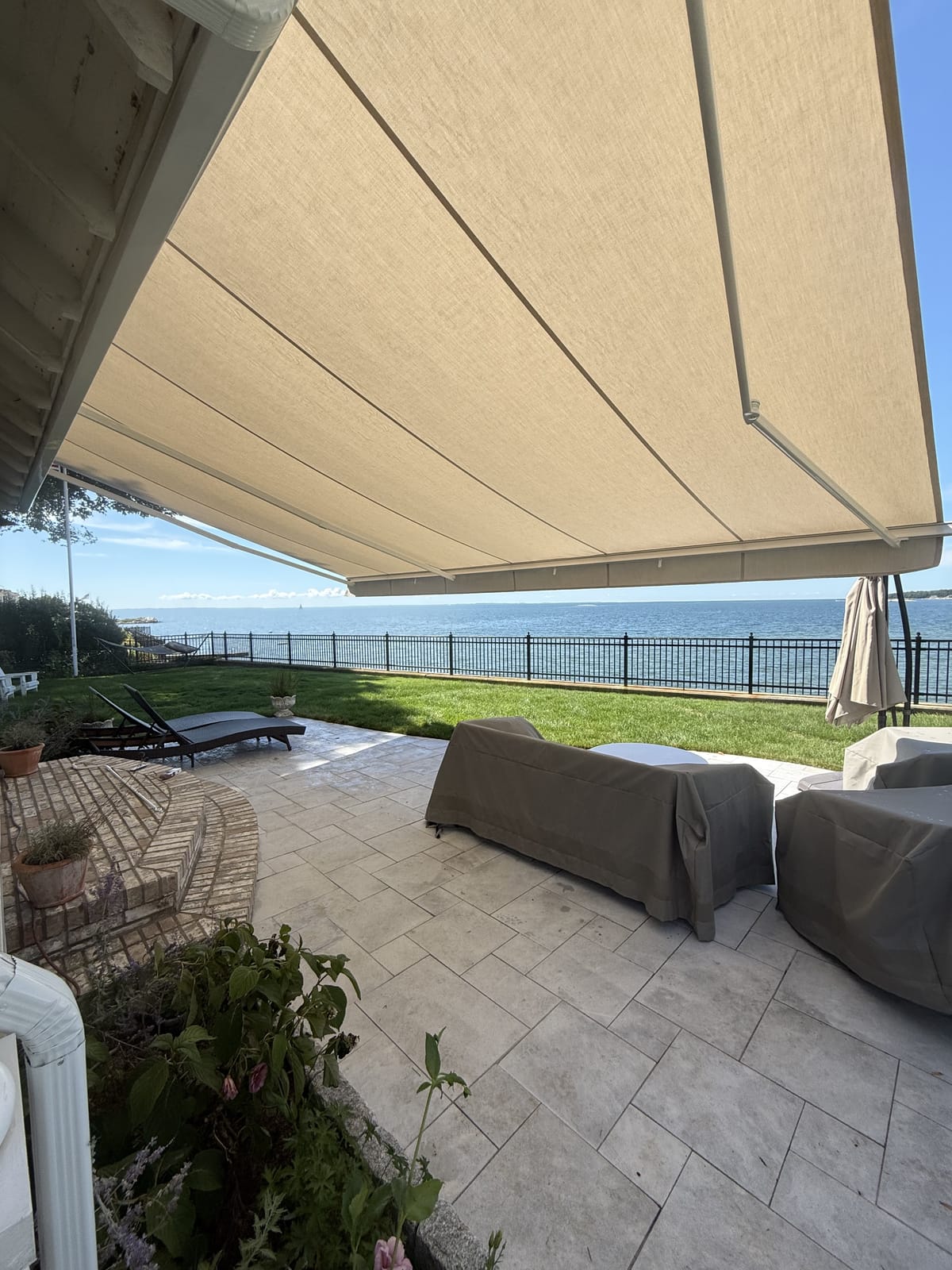 View from beneath a retractable awning overlooking the water at a shorefront patio