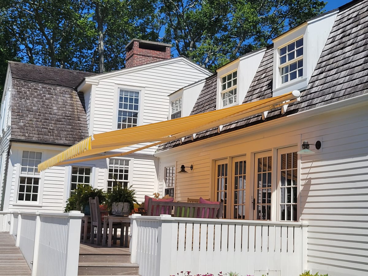 Underside view of a yellow striped retractable awning shading a backyard deck