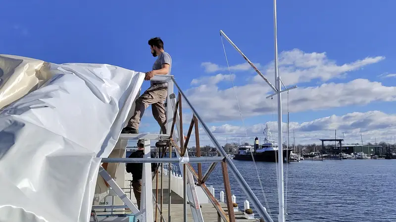 Pease crew member fitting a seasonal canopy cover on a dock frame at a waterfront marina