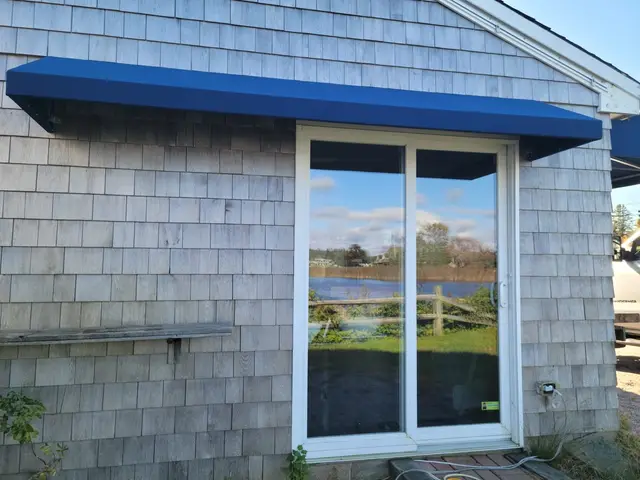 Royal blue shed awning over a slider door on a weathered-shingle waterfront cottage