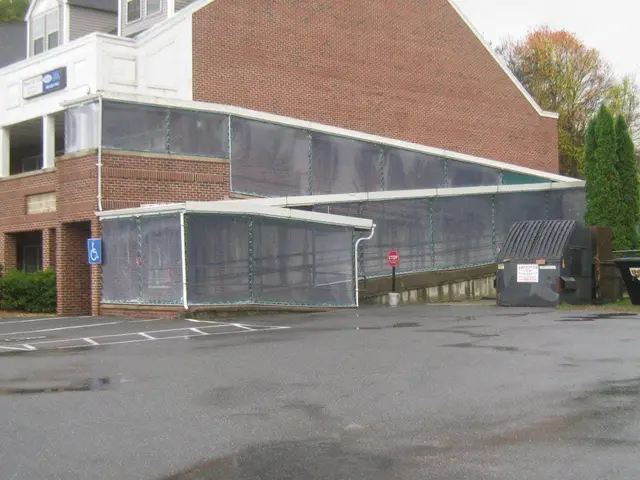 Covered walkway with clear vinyl side curtains along an accessible ramp at a brick commercial building