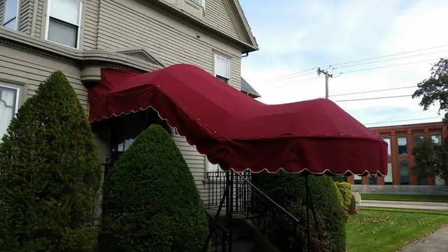 Burgundy scalloped walkway canopy over iron-railed front steps of a Victorian home