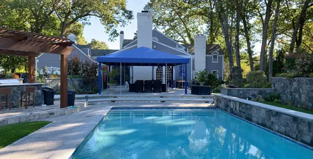 Blue freestanding canopy over poolside dining on a stone backyard terrace