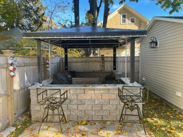 Black flat-roof canopy sheltering a stone outdoor kitchen bar