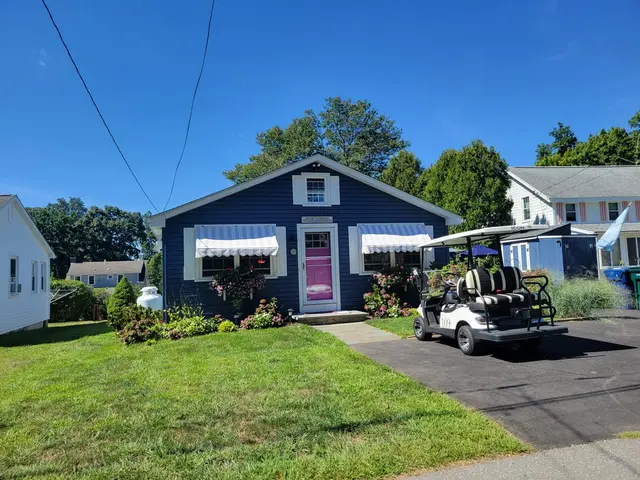 White striped window awnings on a navy beach cottage with a pink front door