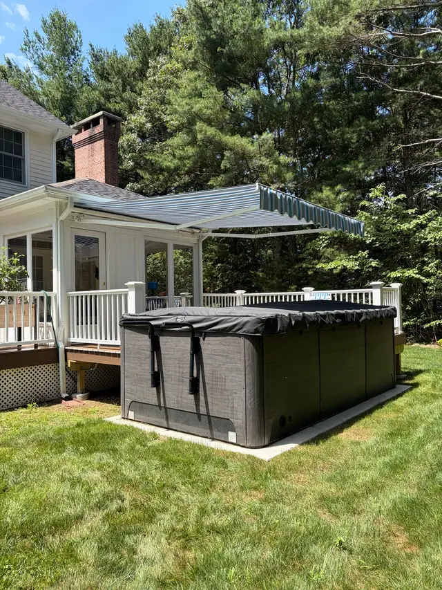 Blue striped retractable awning extended over a backyard deck and hot tub