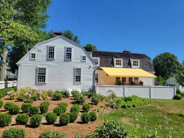 Yellow striped retractable awning extended over the patio of a historic gambrel colonial