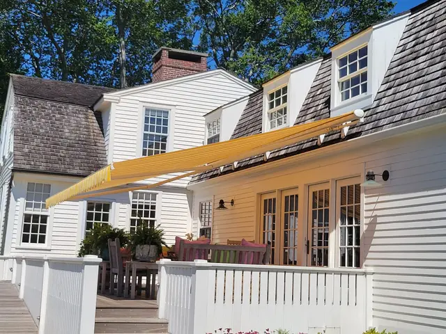 Underside view of a yellow striped retractable awning shading a backyard deck