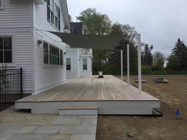 Olive rectangular shade sail stretched over a new wood deck from house to posts