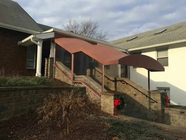 Copper-toned barrel stairwell awning covering the outdoor stone staircase of a brick community building