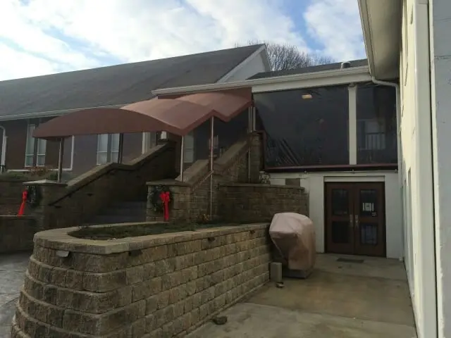 Curved stairwell awning with screened side panels sheltering the steps beside a stone patio entrance