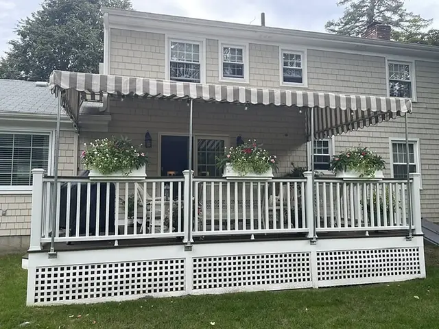 Tan and white striped stationary awning over a rear deck with white railings and flower boxes