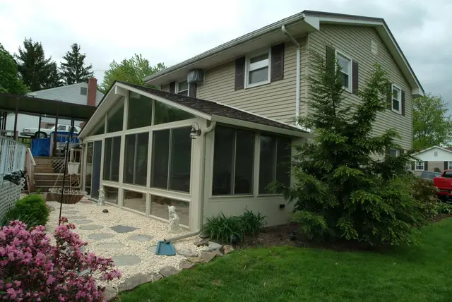 Tan sunroom addition behind a garden hedge and stone path