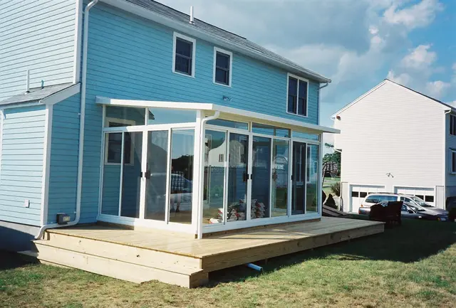 White sunroom on a new deck platform against a sky-blue home