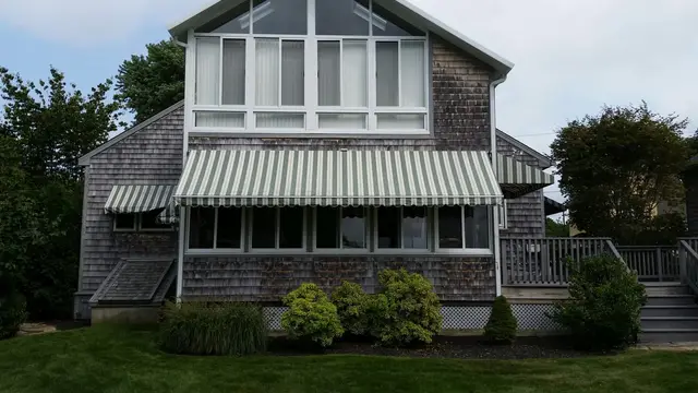 Green striped awnings shading the window wall of a shingled beach house